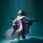 Beautiful woman wearing purple dress freediving in the pool of underwater studio fashion photoshoot