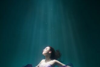 Beautiful woman wearing purple dress freediving in the pool of underwater studio fashion photoshoot