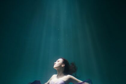 Beautiful woman wearing purple dress freediving in the pool of underwater studio fashion photoshoot