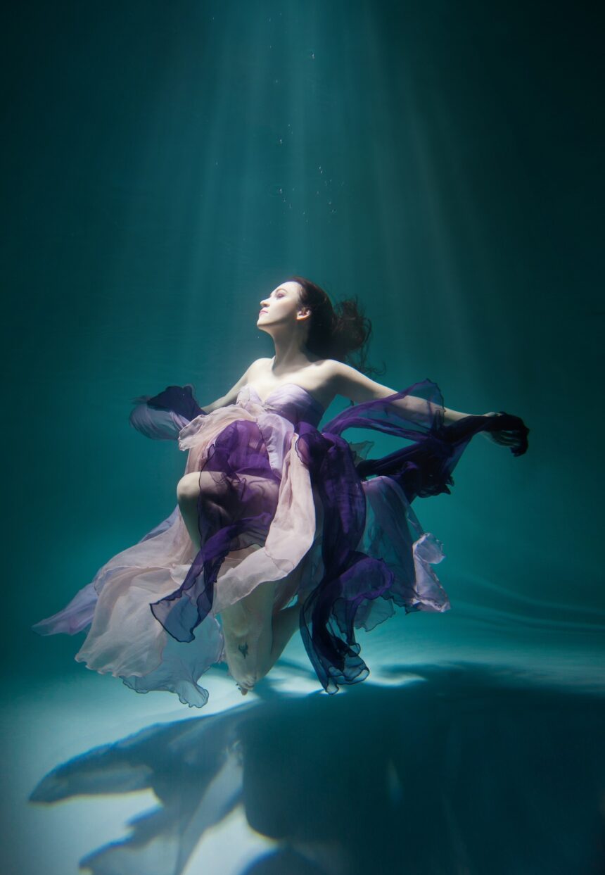 Beautiful woman wearing purple dress freediving in the pool of underwater studio fashion photoshoot