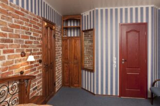 Bed in bedroom with wallpaper and brick wall and wooden cupboards and doors.