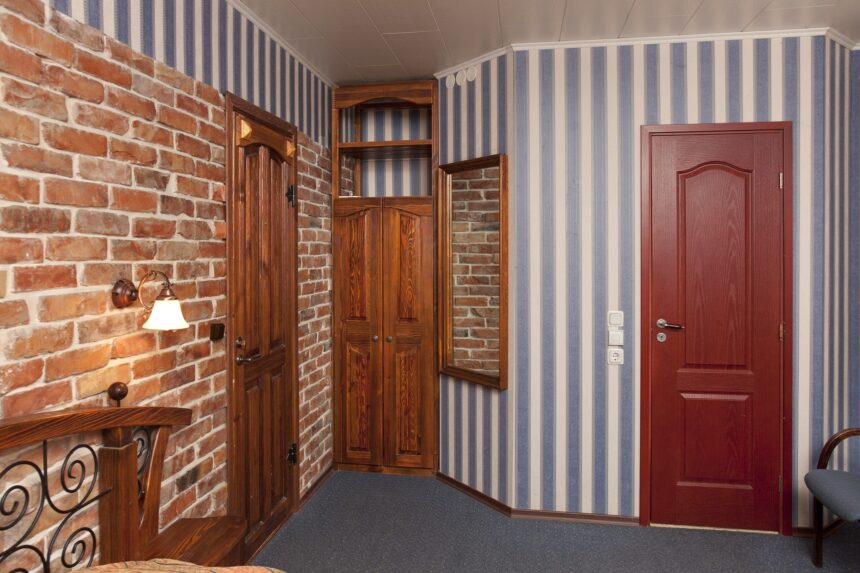 Bed in bedroom with wallpaper and brick wall and wooden cupboards and doors.