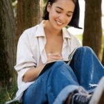 Portrait of happy asian girl sitting in park and writing in her diary. Young woman doing homework