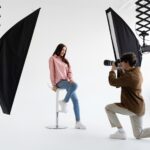 Professional photographer taking picture of young woman, having photoshoot in studio with lighting