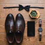 Top view of modern groom's outfit: bow tie, smartphone, wedding rings, watch, leather shoes and bout