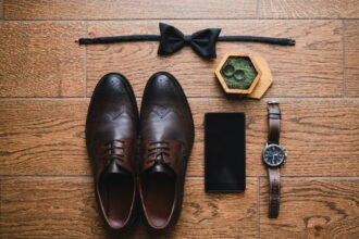 Top view of modern groom's outfit: bow tie, smartphone, wedding rings, watch, leather shoes and bout