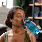 Woman in sporty fitness outfit drinking water after workout at home. Water balance, healthy dieting