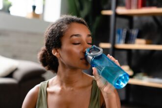 Woman in sporty fitness outfit drinking water after workout at home. Water balance, healthy dieting