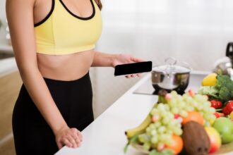 Woman using phone calculating calories on kitchen