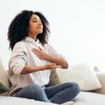 Young woman practicing breathing exercises sitting on sofa at home