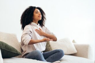 Young woman practicing breathing exercises sitting on sofa at home